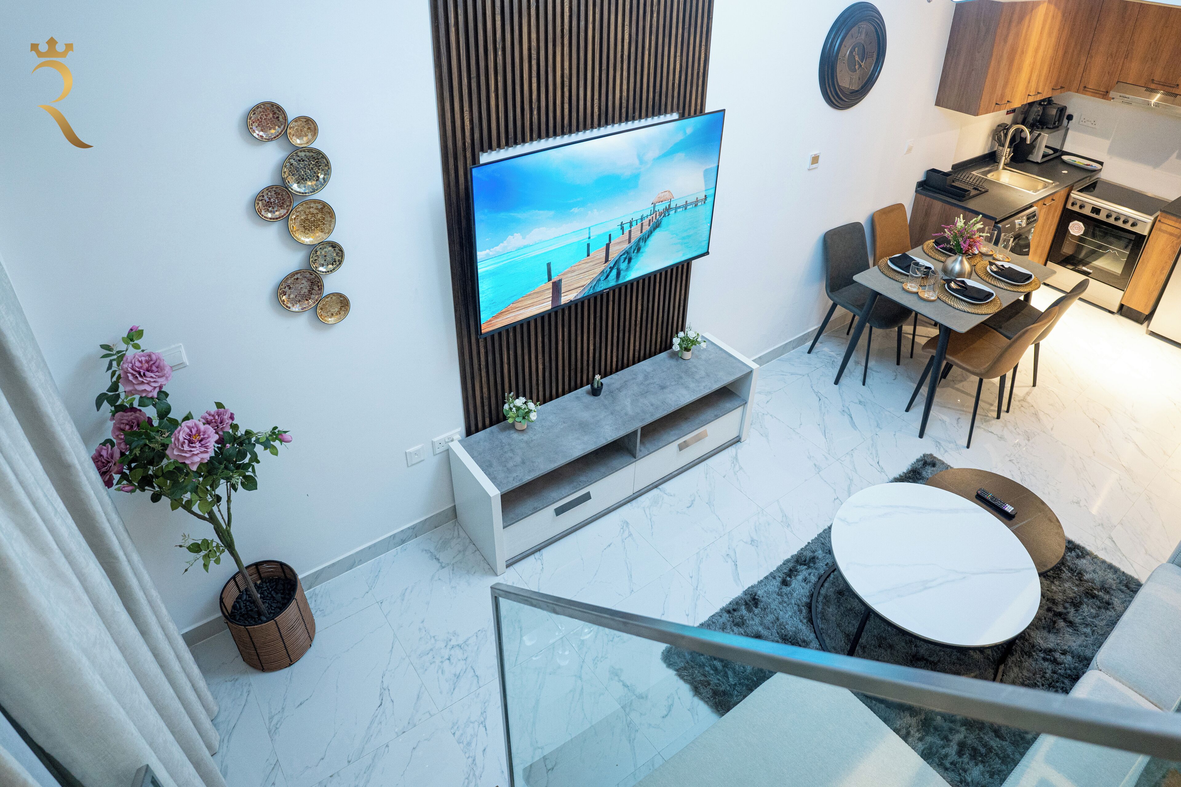 Ett modernt kök med en platt-TV, en matplats med ett runt bord och en trappa med ett glasräcke.