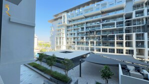 A modern multi-story residential building with balconies, a covered outdoor area with trees, and a clear sky. - Masdar Oasis 1 Modern Apartmenst By Rhh (Abu Dhabi)