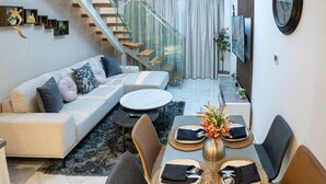A modern living room with a sofa, dining table set for two, and a staircase. - Masdar Oasis 1 Modern Apartmenst By Rhh (Abu Dhabi)
