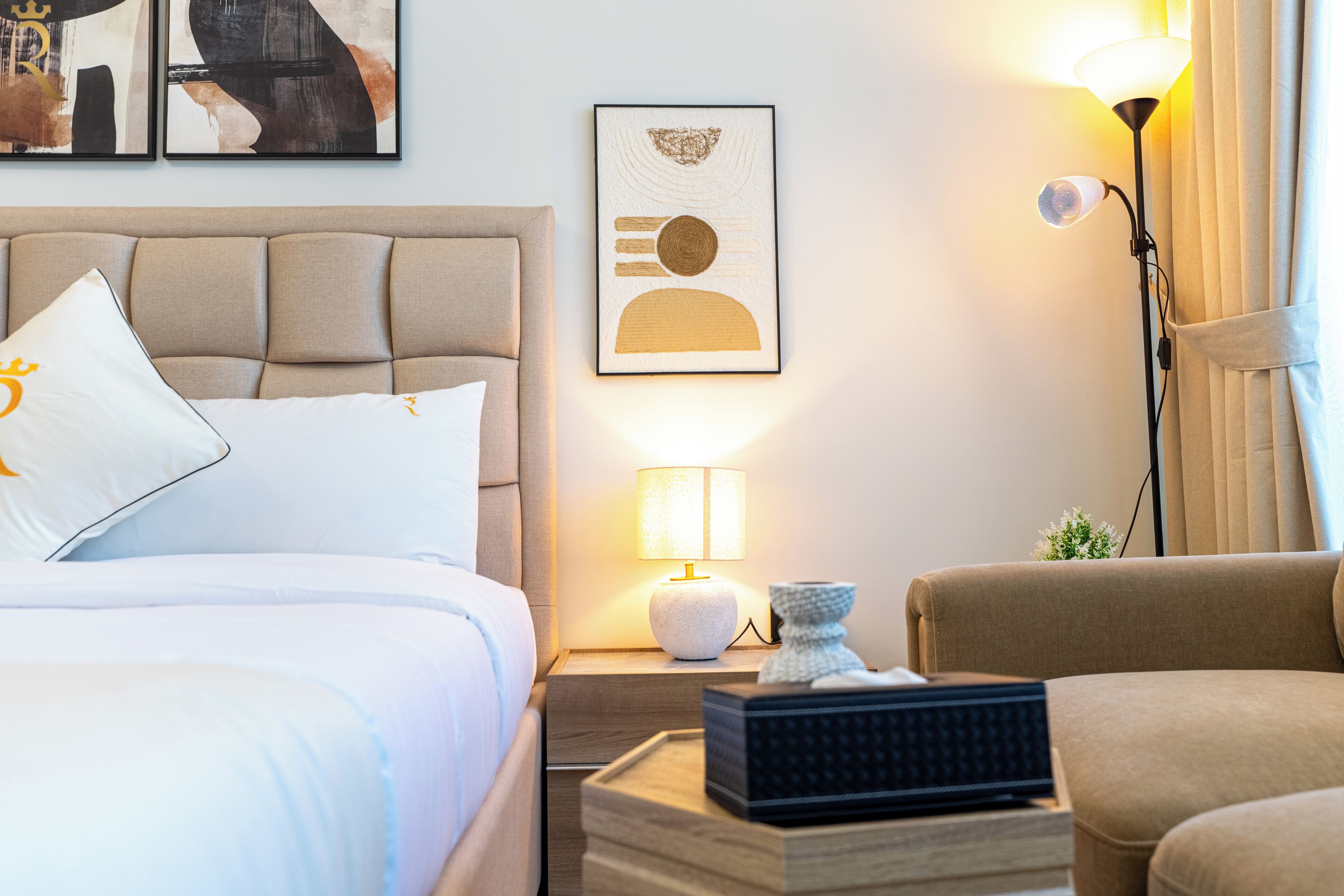 Hotellihuone, jossa on sänky, yöpöytä lampun kanssa, kehystetty taideteos ja sohva.