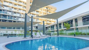 Une piscine moderne, dotée de chaises longues, et un bâtiment avec des balcons en arrière-plan.
