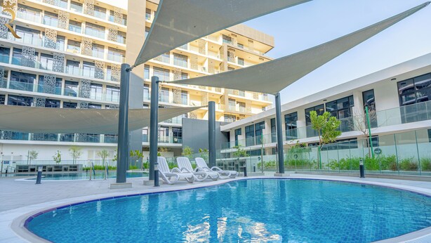 A modern swimming pool with lounge chairs and a building with balconies in the background. - Masdar The Gate Studio (Abu Dhabi)