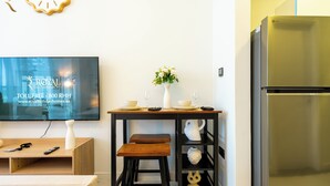 Une cuisine moderne avec un réfrigérateur en acier inoxydable, une table en bois accompagnée de deux tabourets, un vase rempli de fleurs et un téléviseur à écran plat fixé au mur.