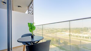 A balcony with a table and chairs, a potted plant, and a view of a cityscape. - Masdar The Gate Studio (Abu Dhabi)