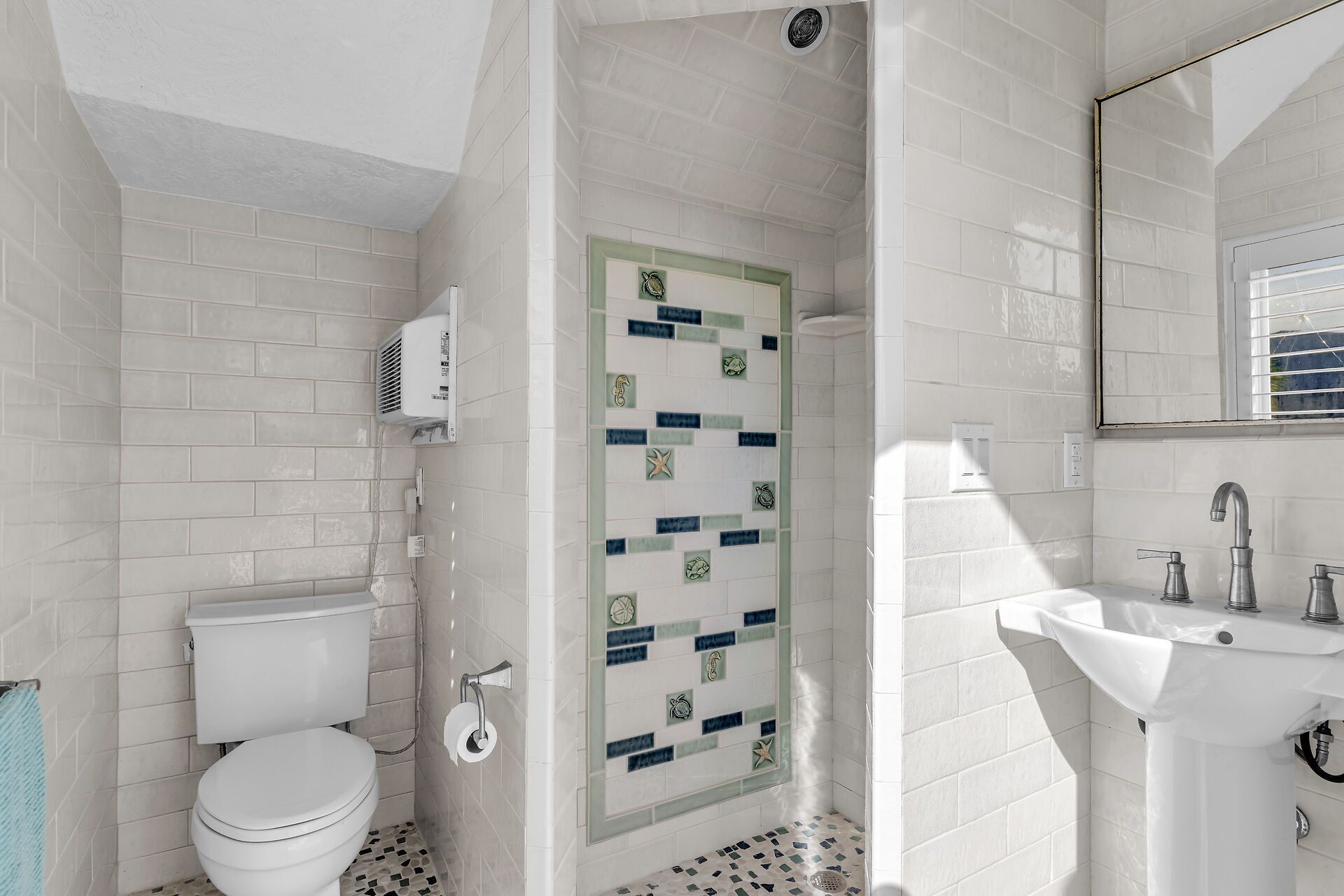 Une salle de bain avec des carreaux blancs, des toilettes, un lavabo et une douche.