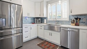 A modern kitchen with white cabinets, stainless steel appliances, a blue-tiled backsplash, and a window with shutters. - Fabulous 2-bedroom house with Pool and spa in sunny Long Beach (Long Beach)
