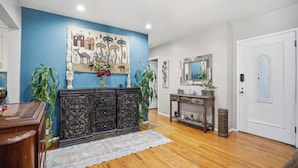 A room with a blue accent wall, wooden floor, a large painting, a dark wooden cabinet, a small table with decorative items, and a white door. - Fabulous 2-bedroom house with Pool and spa in sunny Long Beach (Long Beach)