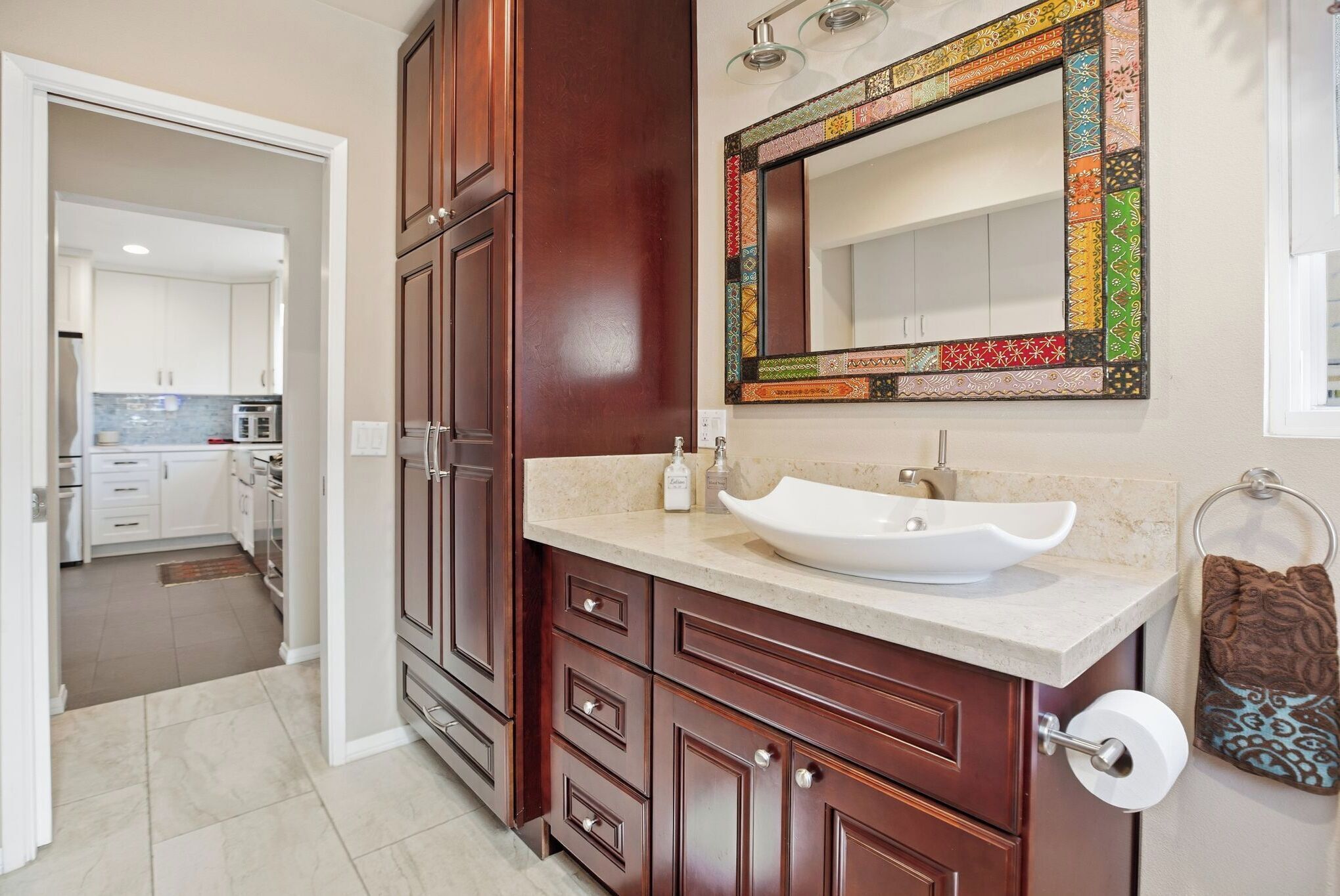 A bathroom with a large mirror, wooden cabinets, a white sink, and a towel rack.