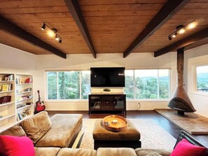 A living room with a TV, bookshelves, a fireplace, and a large window with a view. - 4 Bed Sunset Abode with Open-Plan & Stunning Views (Los Angeles)