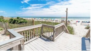 Een houten terras leidt naar een strand met parasols en mensen.