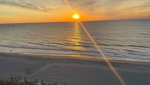 Een strand bij zonsondergang, met de zon die in het water weerspiegelt, een hek en begroeide duinen.