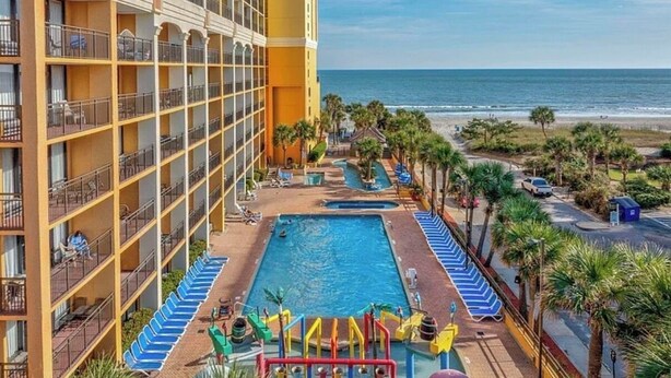 Hotel met zwembadgedeelte, inclusief glijbaan en ligbedden, met uitzicht op een strand.