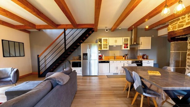 Une cuisine moderne avec des meubles blancs, un réfrigérateur en acier inoxydable et une table à manger en bois, accompagnée de chaises.