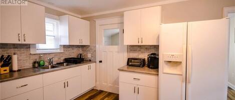 A kitchen with white cabinets, a microwave, a toaster, and a refrigerator.