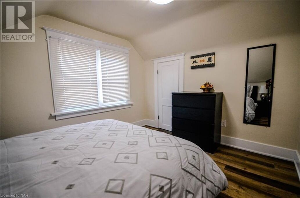 A bedroom with a bed, dresser, window with blinds, door, and a mirror on the wall.