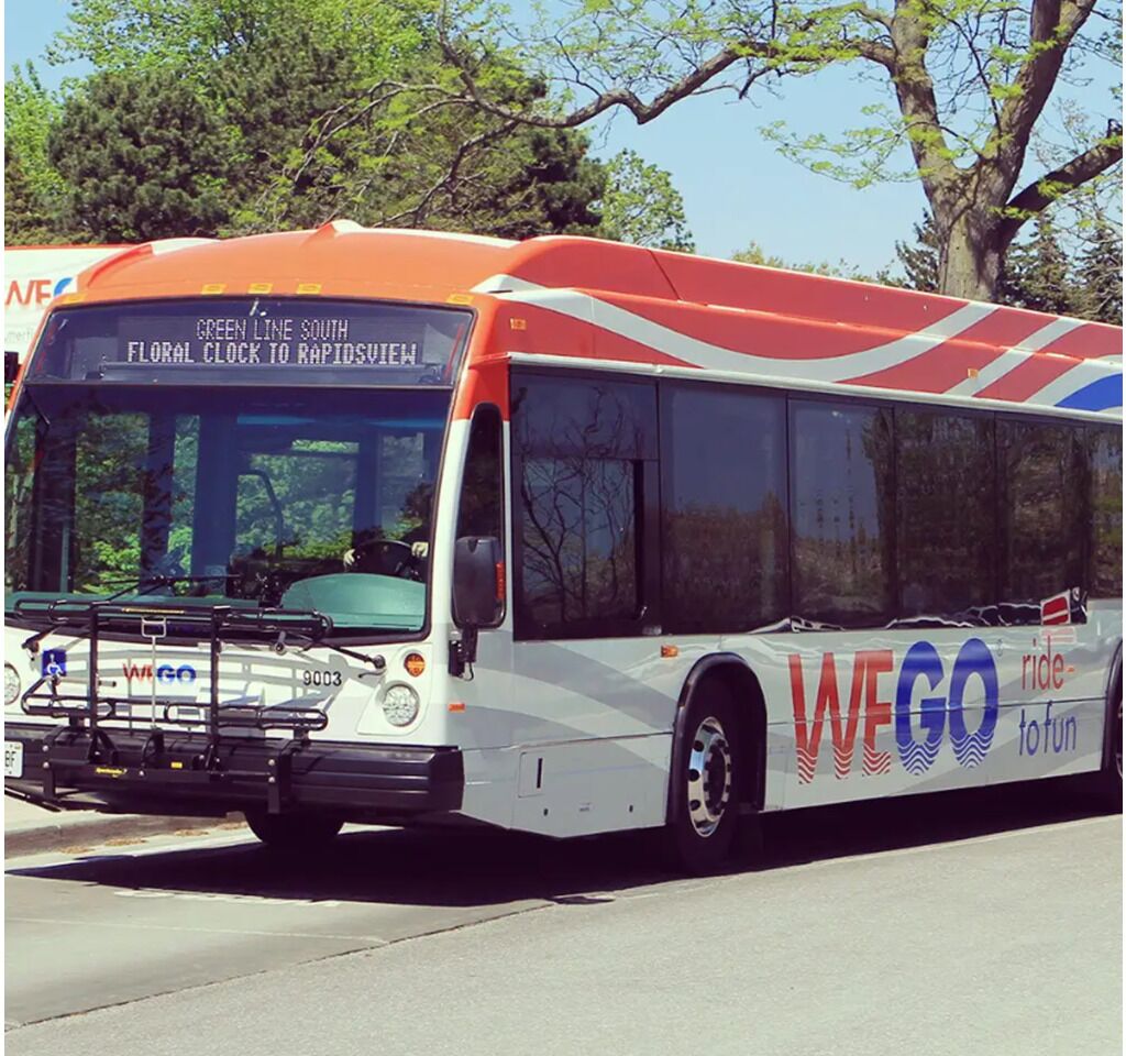 A public transit bus with "WIGO ride to fun" branding, parked on a street with trees in the background.