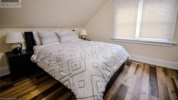 Un dormitorio con cama, dos mesitas de noche con lámparas, una ventana con persianas y suelo de madera.
