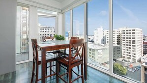 Un espace repas moderne avec une table en verre et des chaises en bois, de grandes fenêtres offrant une vue sur la ville.