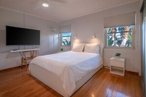 A modern bedroom with a large bed, a flat-screen TV, a desk, and a window with a view of palm trees. - Palm Springs ~ Pool, Hot Tub (Palm Springs)