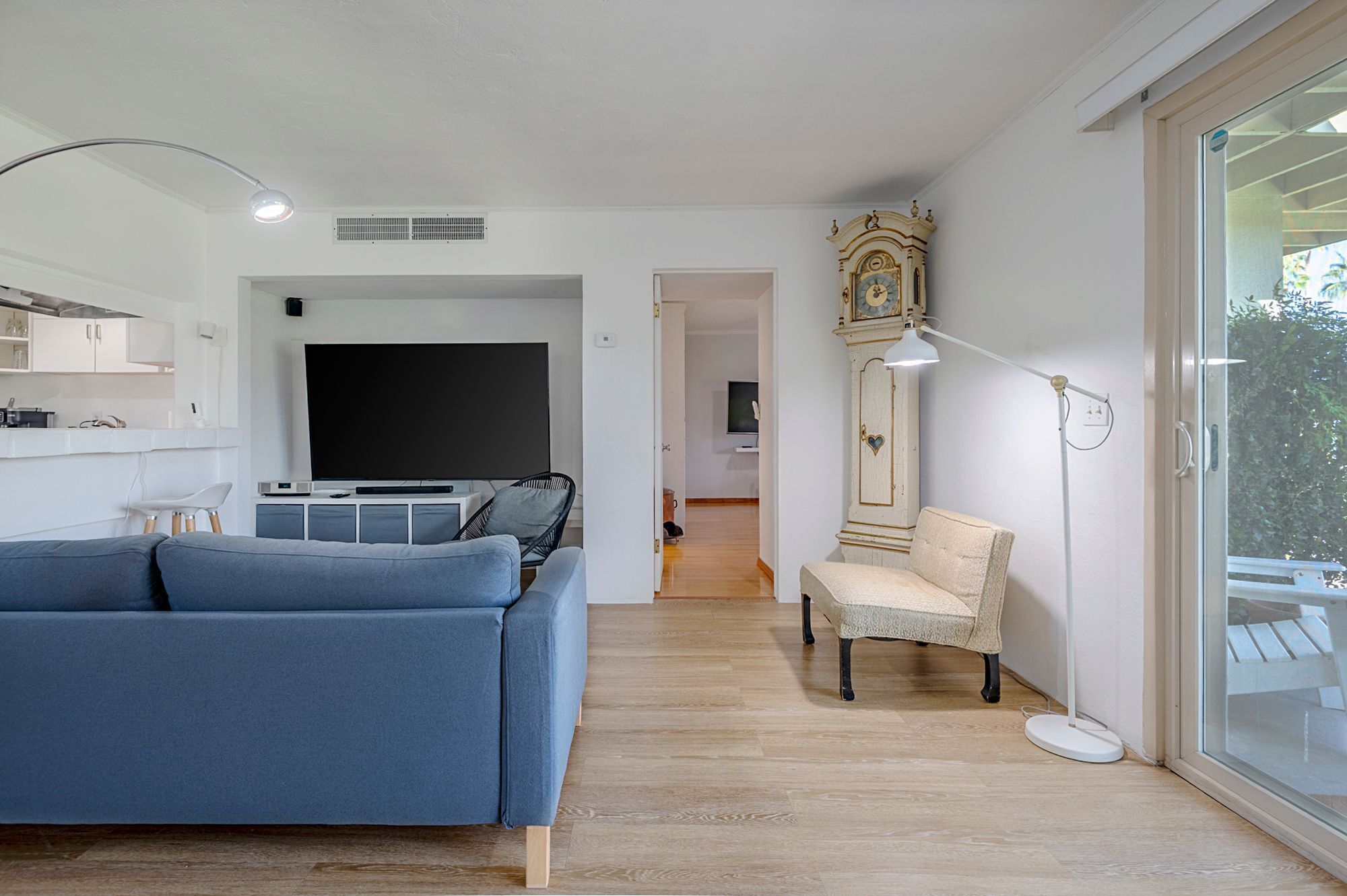 Un salon moderne avec un canapé bleu, un téléviseur à écran plat, une horloge ancienne et une grande fenêtre.