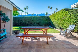 A patio with a wooden table and bench, surrounded by a well-maintained hedge and a view of mountains. - Palm Springs ~ Pool, Hot Tub (Palm Springs)