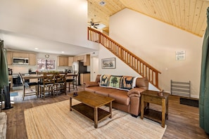 A spacious living room with a wooden staircase, a dining area, and a kitchen with wooden cabinets and a microwave. - Noble Estates Cabin, Luxe Forest Escape (Nutrioso City)