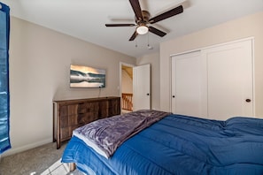 A bedroom with a bed, a ceiling fan, a wooden dresser, a painting, and a door leading to another room. - Noble Estates Cabin, Luxe Forest Escape (Nutrioso City)