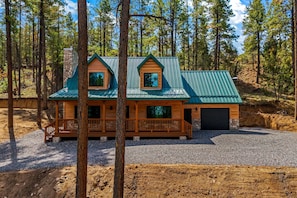 A cabin with a green metal roof, wooden deck, and a stone chimney. - Noble Estates Cabin, Luxe Forest Escape (Nutrioso City)