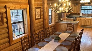 Een chalet inrichting met een eettafel, stoelen, een kroonluchter en een keukenhoek.