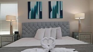 Ein ordentlich bezogenes Bett mit einer herzförmigen Handtuchgestaltung, einem mit Wirbeln verzierten Kopfteil und zwei abstrakten Bildern an der Wand.
