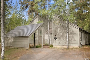 Exterior of a wood-sided house with a metal roof and attached carport in the trees. - Black Butte Ranch Golf Home 155 (Sisters)
