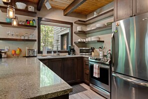 Kitchen with stainless steel appliances, dark cabinets, and floating wood shelves. - Black Butte Ranch Golf Home 155 (Sisters)