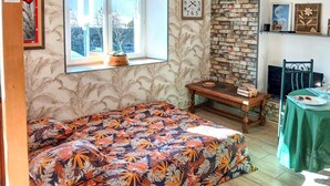 Een knus ingerichte kamer met een bed, een klein tafeltje, een klok en een raam met uitzicht op het omliggende landschap.