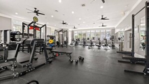 A spacious gym with ceiling fans, various exercise equipment, and large windows allowing natural light. - Serene Bliss: Stylish 1BR Unit in Resort Complete (Jacksonville, Florida 32224)