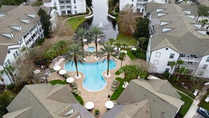 An aerial view of a residential area with a swimming pool surrounded by palm trees and lounge chairs, indicating a resort-like setting. - Serene Bliss: Stylish 1BR Unit in Resort Complete (Jacksonville, Florida 32224)
