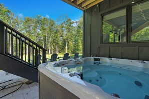 A hot tub on a wooden deck with a view of trees, a railing, and a window. - Lakefront Scandinavian Vacation Rental with Private Dock, Hot Tub & Kayaks<br> Brand New, modern home with high end amenities - close to Ogunquit, Kennebunkport and Wells Beaches. (Alfred)