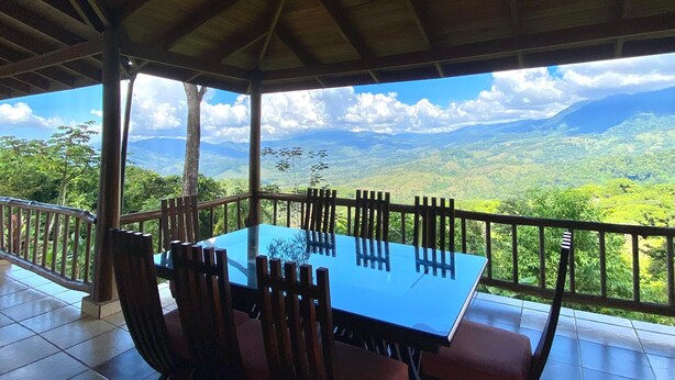 Ein Essbereich im Freien mit Tisch und Stühlen, einem Deckenventilator und Blick auf eine gebirgige Landschaft.