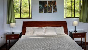 Ein Schlafzimmer mit Holzboden, einem Bett mit gesteppter Matratze, zwei Nachttischen mit Lampen und einem Fenster mit Vorhängen.