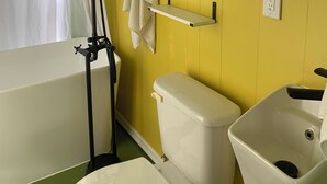 Kylpyhuone, jossa on keltainen seinä, valkoinen wc-istuin, valkoinen pesuallas, kylpyamme ja suihkuverho.