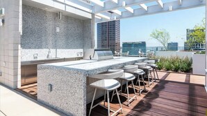 Un'area cucina esterna con piano di lavoro in granito, sgabelli da bar e struttura a pergola.