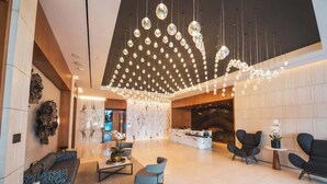 Una hall moderna con una scrivania della reception in marmo, sedute nere e un lampadario con luci pendenti.