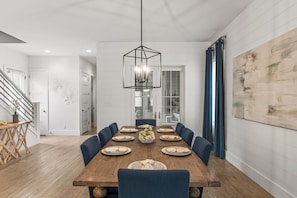 Ein Esszimmer mit einem Holztisch, gedeckt für sechs Personen, umgeben von blauen Stühlen, einer hängenden Leuchte und einem großen, abstrakten Gemälde an der Wand.