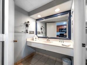 A bathroom with a large mirror, two sinks, towel dispensers, and a trash can. - Landmark 633 (Myrtle Beach)