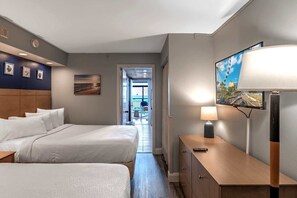 A hotel room with two beds, a desk with a lamp, a TV, and a painting on the wall. - Landmark 633 (Myrtle Beach)
