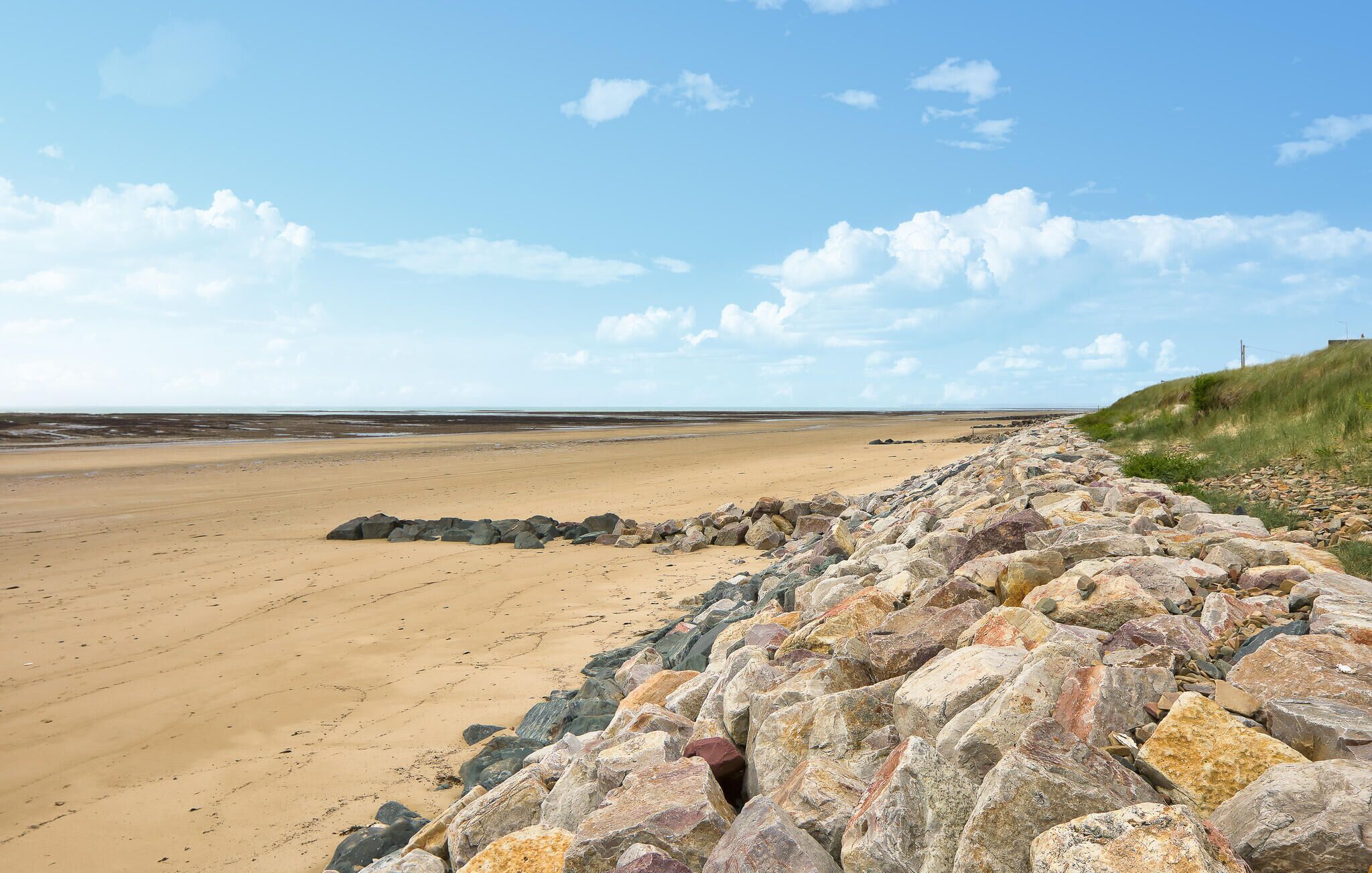 Ein Strand mit einem steinernen Wellenbrecher und blauem Himmel.