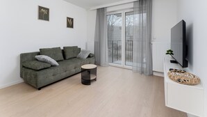 Een moderne woonkamer met een grijze bank, een klein rond tafeltje, een plafondlamp en een aan de muur bevestigde televisie.