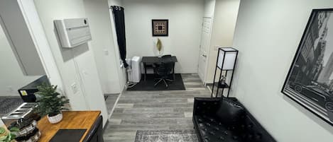 Un espacio habitable compacto con comedor, un sofá negro, una pequeña oficina y una alfombra estampada.