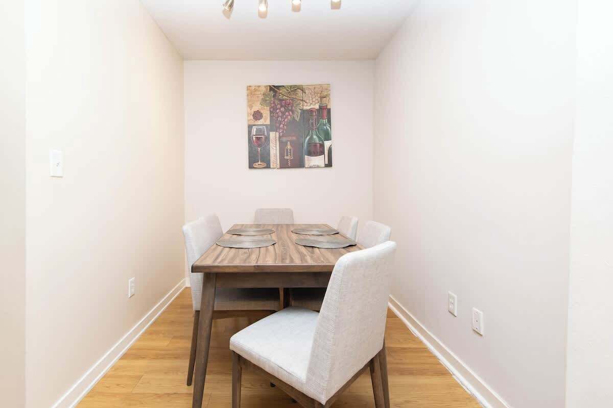 Un comedor con una mesa de madera y cuatro sillas, un cuadro en la pared y un interruptor de luz.