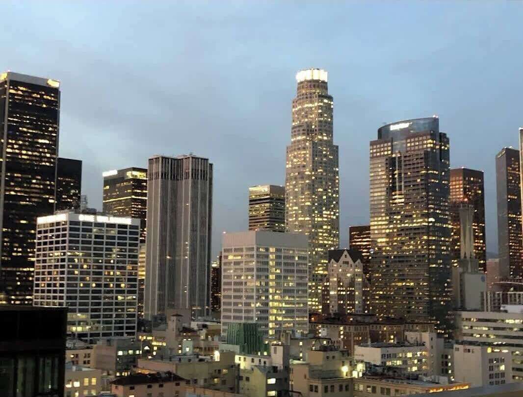 A cityscape with multiple high-rise buildings, some with illuminated windows, indicating a downtown area.