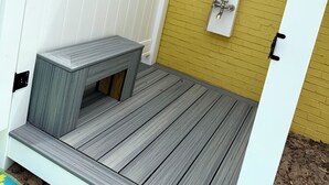 Un petit espace de douche extérieur, à l’abri, avec une terrasse en bois, une porte blanche et un mur en briques jaunes.